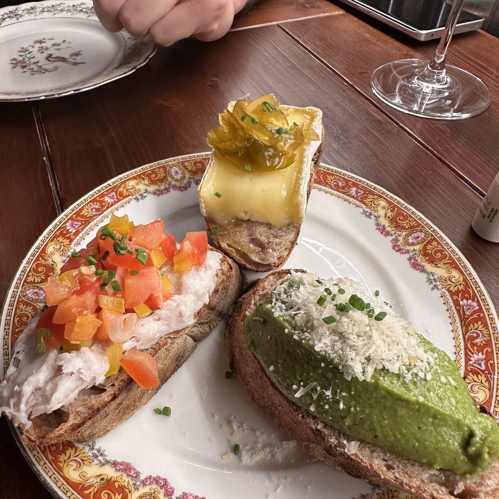 Tre cicchetti su un piatto decorato: pane con polpa di granchio e pomodoro, pane con formaggio fuso e mostarda, pane con crema di piselli e formaggio grattugiato.