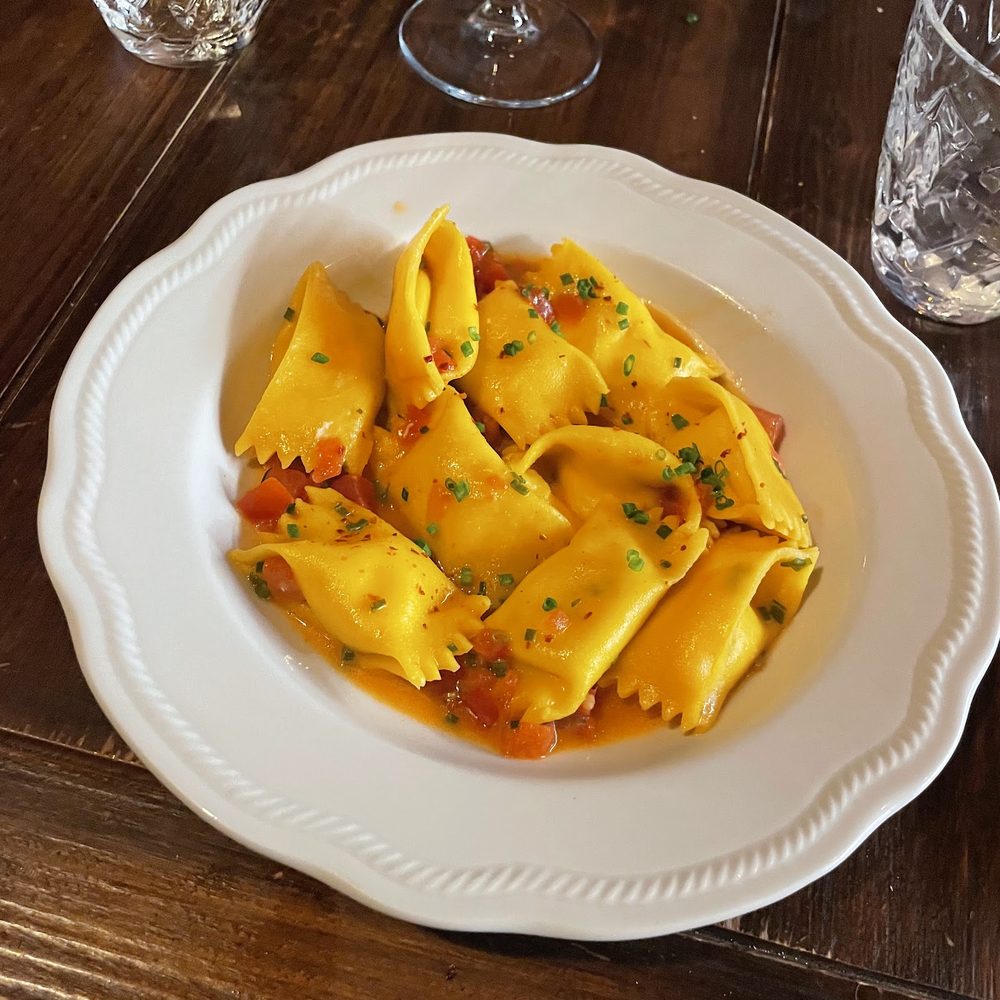 Fazzoletti di pasta fresca gialla in un fondo di burro e pomodoro fresco a dadini, con erba cipollina, in un piatto bianco.