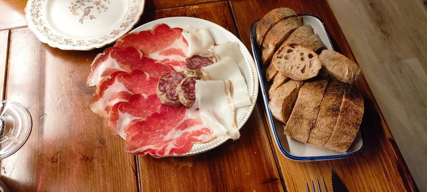 Tagliere di salumi locali: coppa, lardo e salame su un piatto di ceramica antica, con pane a fette in un vassoio smaltato.